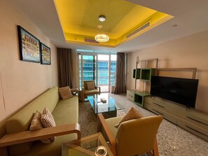 A hotel room with a sofa, armchairs, a coffee table, a flat-screen TV, and a large window with a view of buildings. - VESTA  - Superior Suite - 2BR - Nile View (Cairo)