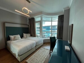 A hotel room with a bed, a desk, and a view of a building through large windows. - VESTA  - Superior Suite - 2BR - Nile View (Cairo)