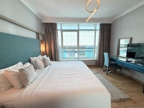 A hotel room with a large bed, a desk with a chair, a television, and a view of the city through the window. - VESTA  -  Executive Suite - 2BR - Nile View (Cairo)