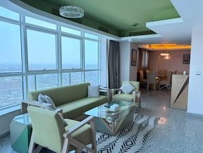 A modern hotel room with a large window, a sofa set, a glass coffee table, and a dining area. - VESTA  -  Executive Suite - 2BR - Nile View (Cairo)