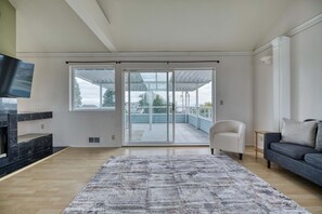Ein geräumiges Wohnzimmer mit einer großen Glasschiebetür, die auf einen Balkon führt, einem an der Wand befestigten Flachbildfernseher, einem grauen Sofa und einem gemusterten Teppich.