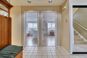 Corredor com cama, escada e vista para uma cozinha e sala através de portas abertas.