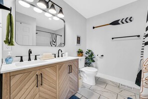 Uma casa de banho moderna com toucador de madeira, um espelho grande e um chuveiro com barra preta.