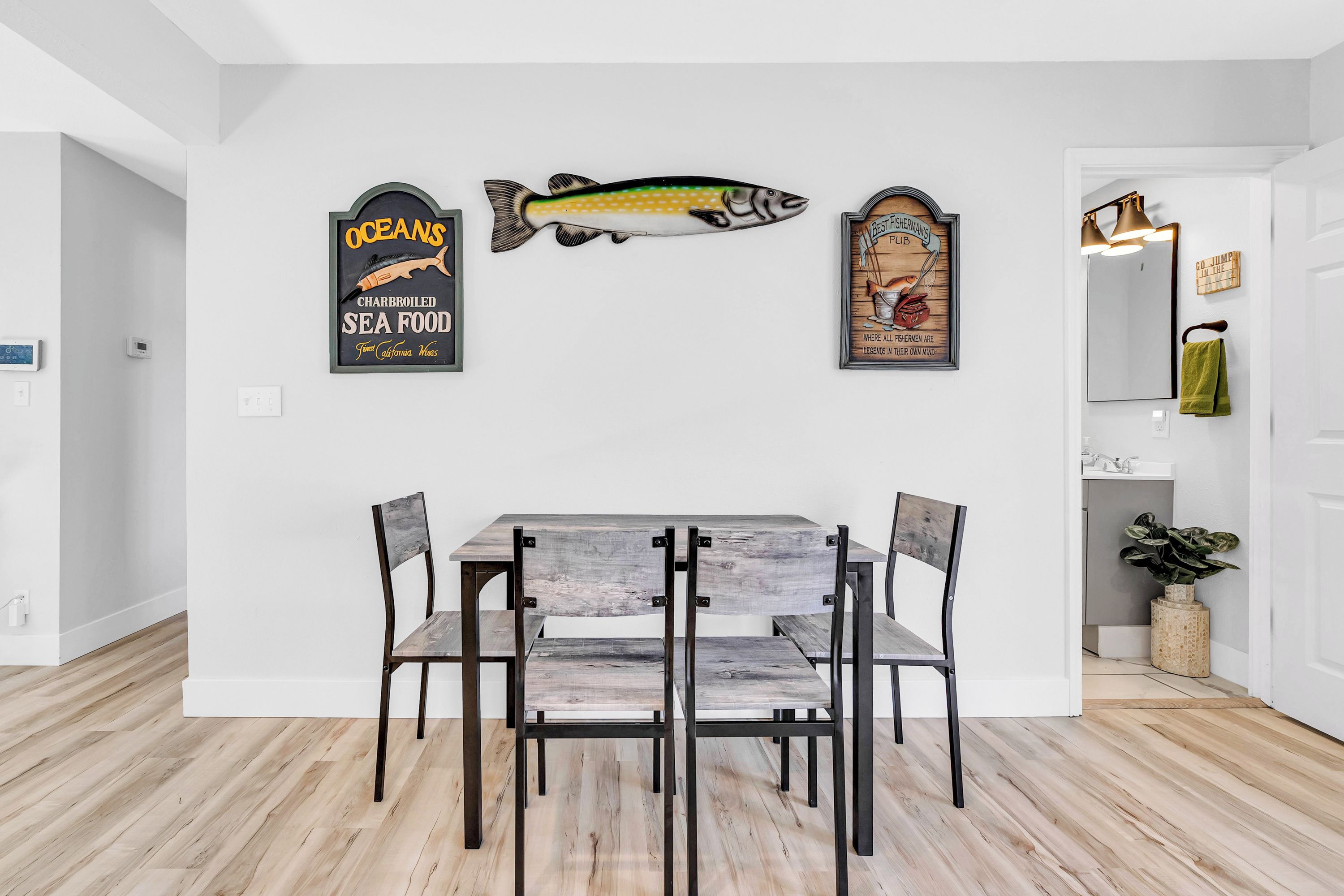 Un comedor con una mesa y sillas de madera, un adorno mural con motivos de peces y un espejo con una toalla.