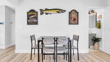 Un comedor con una mesa y sillas de madera, un adorno mural con motivos de peces y un espejo con una toalla.