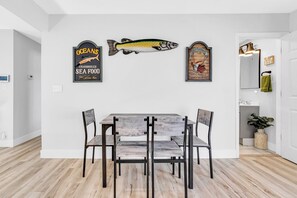 Un comedor con una mesa y sillas de madera, un adorno mural con motivos de peces y un espejo con una toalla.