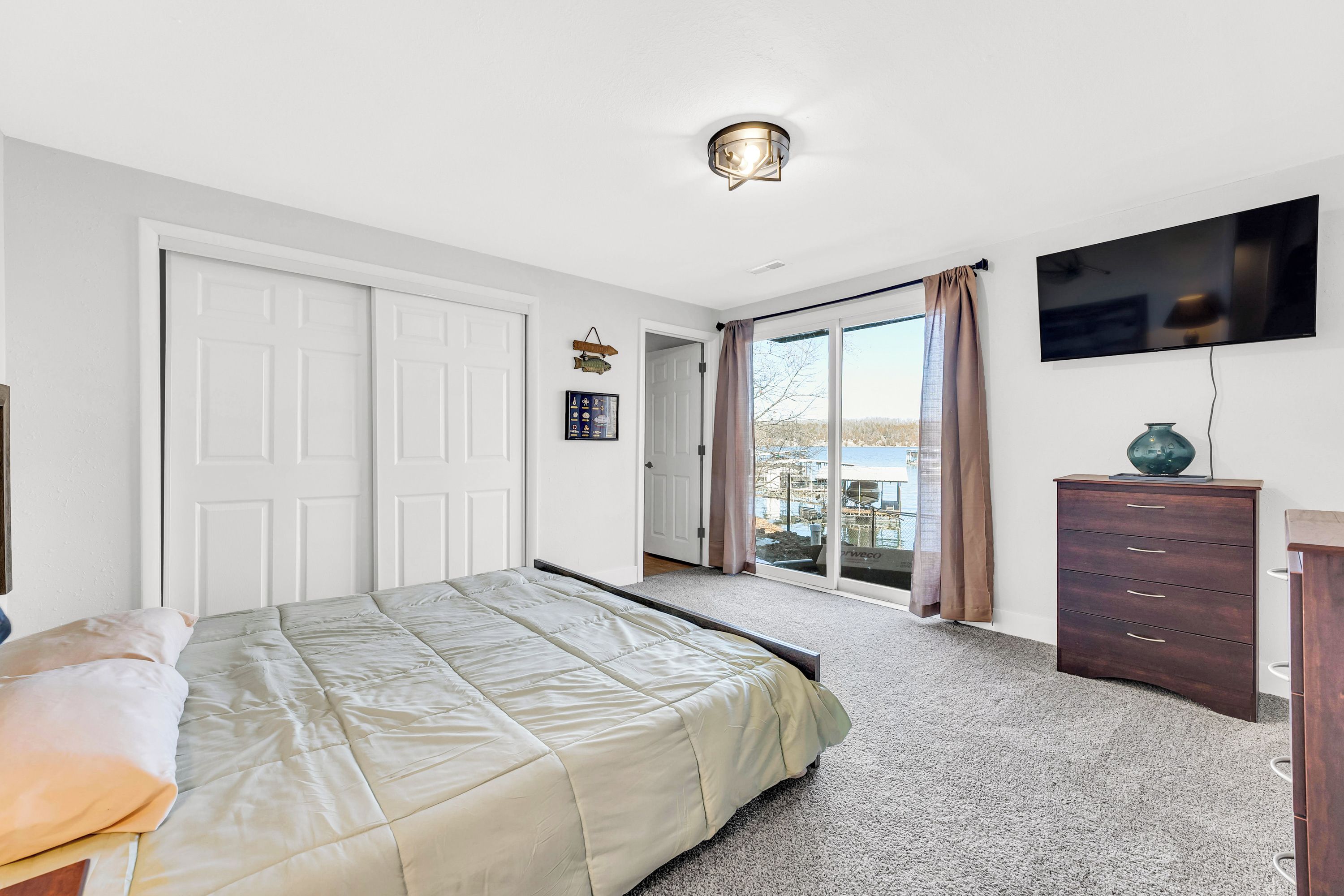A bedroom with a bed, a dresser, a television, and a sliding glass door leading to a balcony.