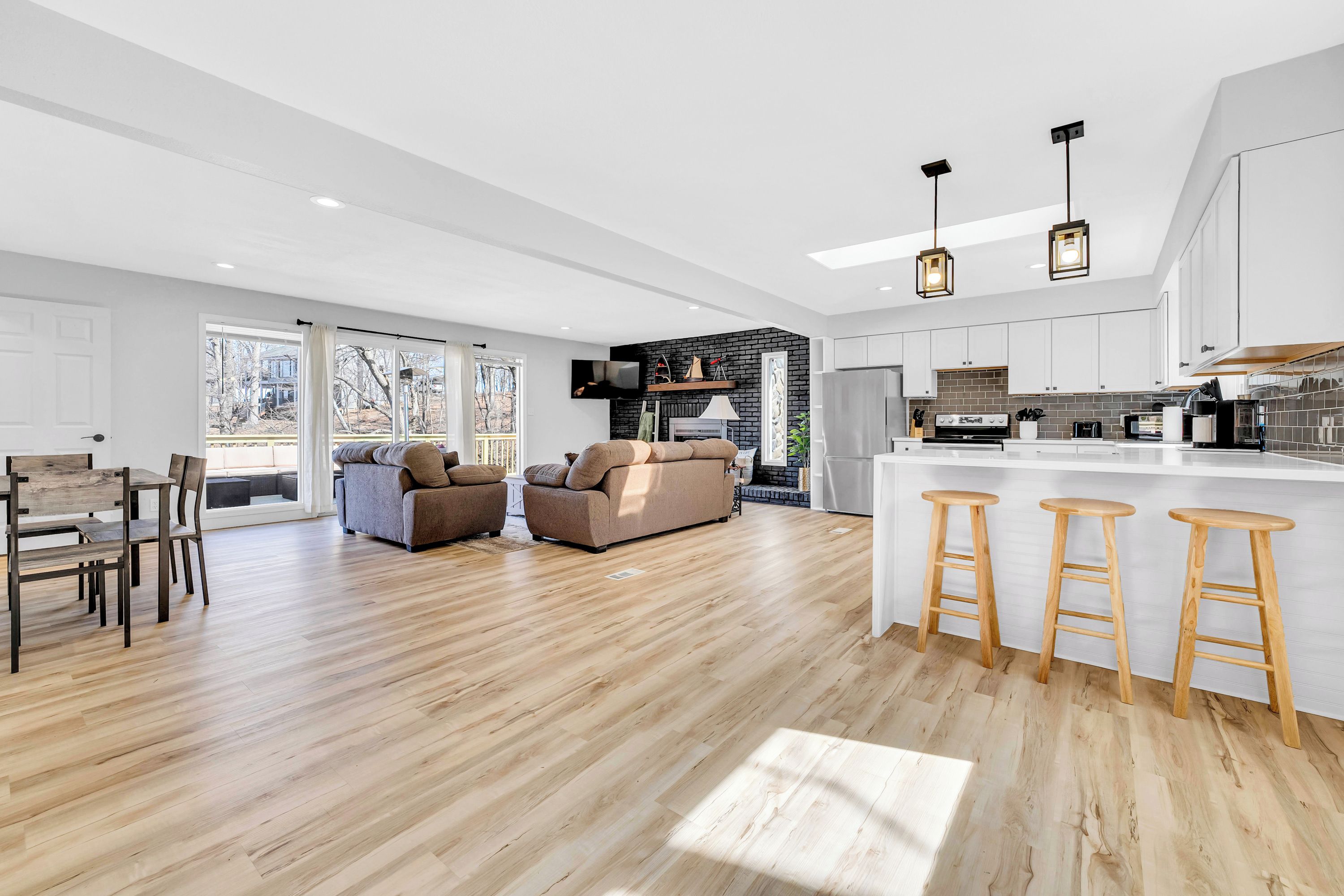 Un salón amplio con piso de madera, un sofá, una mesa de comedor y una cocina con encimera blanca y taburetes de madera.