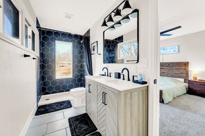 A modern bathroom with a hexagonal tile backsplash, a white vanity with a wooden cabinet, a large mirror, and a window with a view of a building. - Amazing Location~Game Room~Swim Dock~Boat Rental! (Osage Beach)
