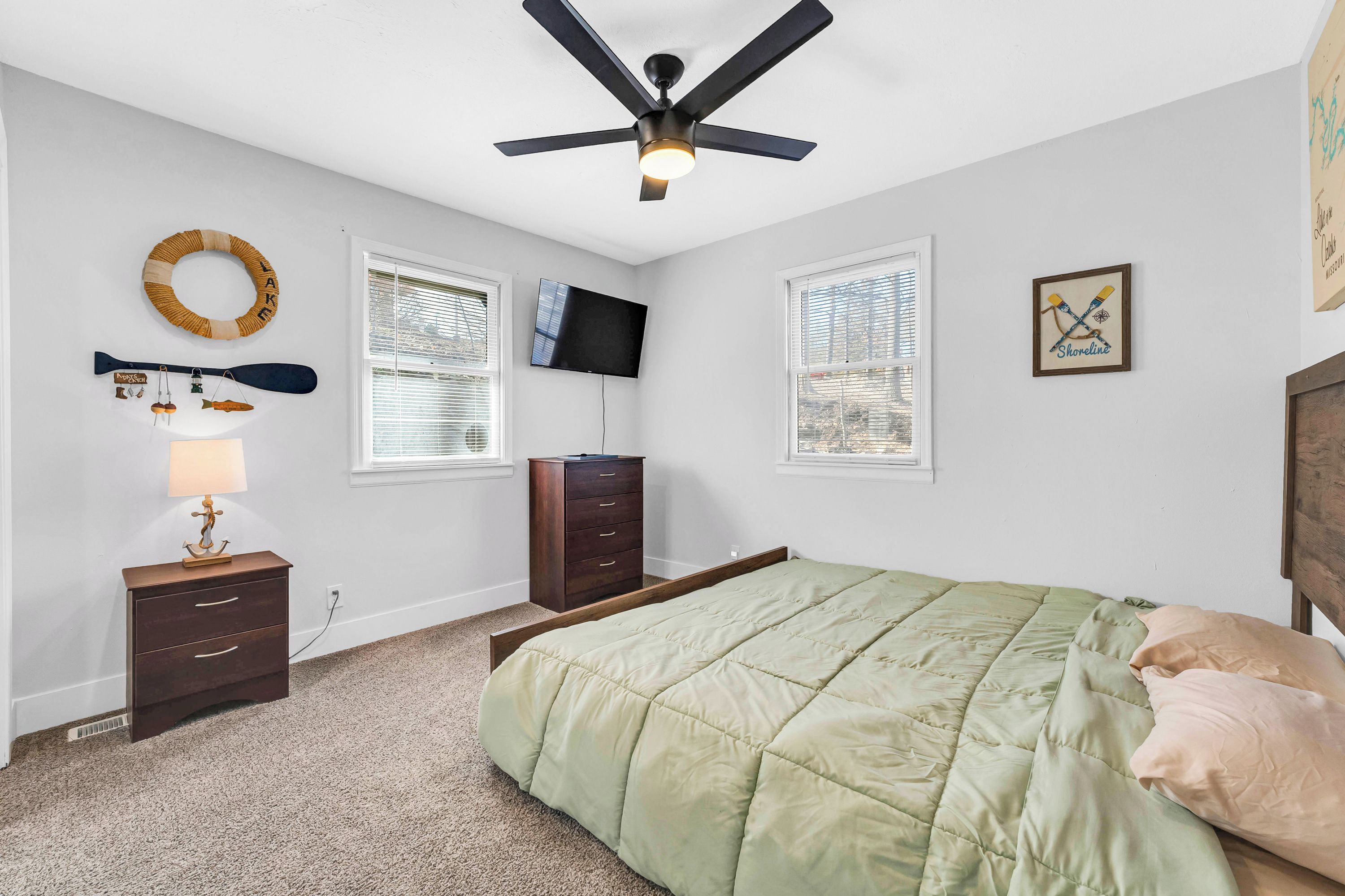 A bedroom with a bed, a ceiling fan, a TV, a dresser, a lamp, and a window with blinds.