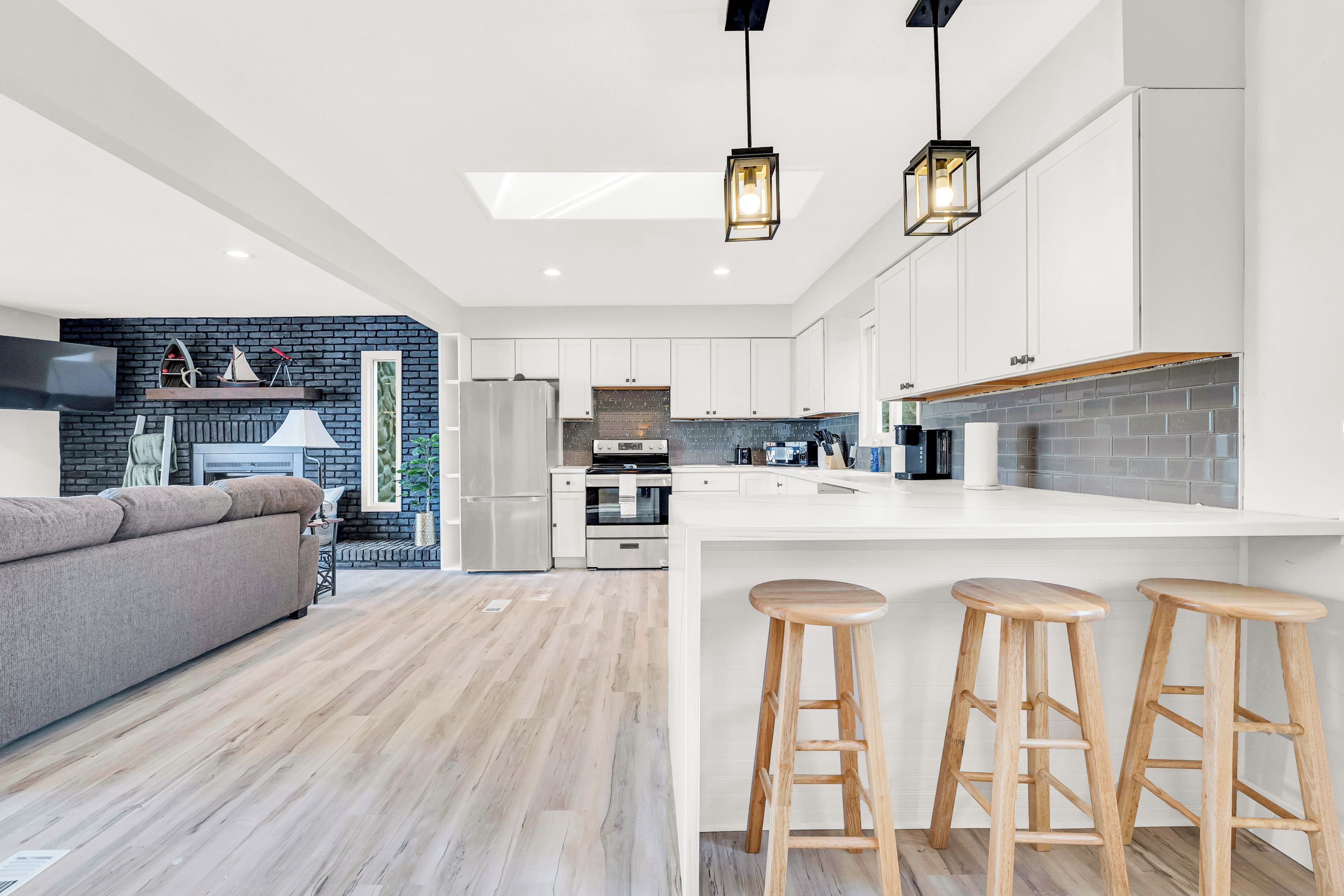 A modern kitchen with white cabinets, a large island with stools, a built-in oven, and a brick accent wall.