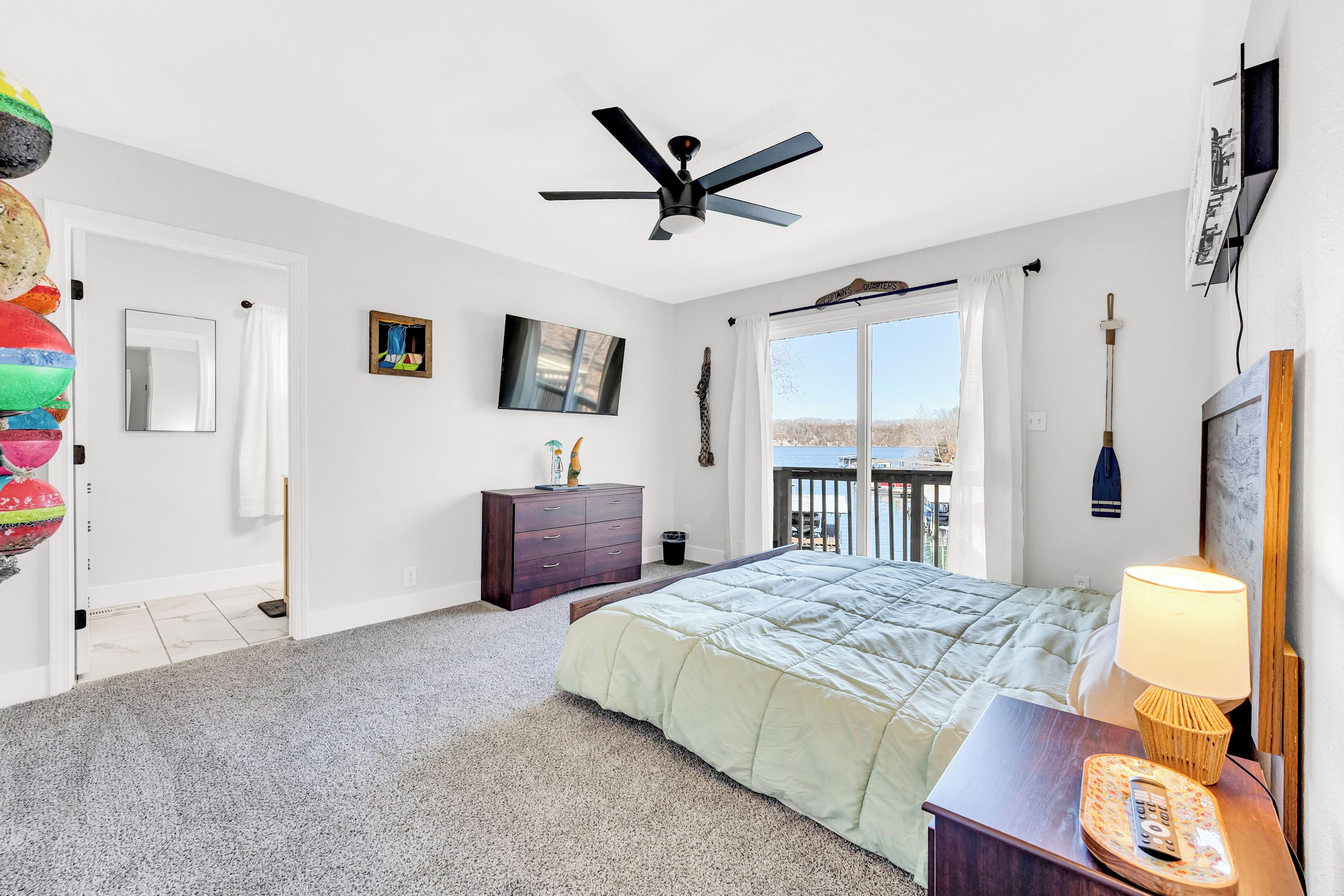A bedroom with a bed, a dresser, a ceiling fan, a TV, and a balcony with a view.