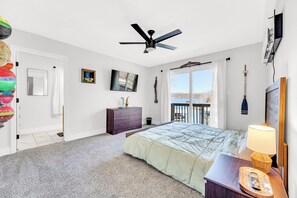 Une chambre à coucher comprenant un lit, une commode, un ventilateur de plafond, une télévision et un balcon avec vue.