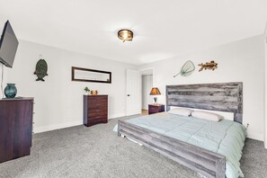 Quarto com cama, cômoda, TV e objetos decorativos.