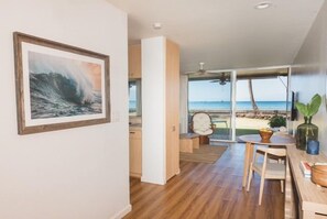 A modern interior with a wooden floor, a dining area with a table and chairs, and a large window offering a view of the beach. - New unit to rent.  Adorable 1 bed/1 bath condo. (Lahaina)