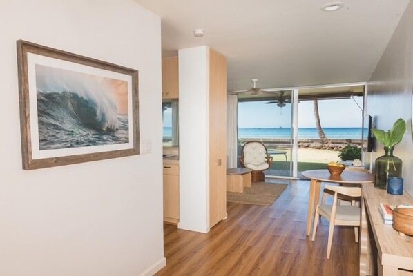 Ein modernes Interieur mit Holzboden, einem Essbereich mit Tisch und Stühlen sowie einem großen Fenster mit Blick zum Strand.