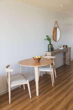 A dining area with a round wooden table, two chairs, a bowl of fruit, a wooden bench, a mirror, and a potted plant. - New unit to rent.  Adorable 1 bed/1 bath condo. (Lahaina)
