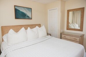 A hotel room with a bed, a nightstand, a dresser, a painting, and a mirror. - New unit to rent.  Adorable 1 bed/1 bath condo. (Lahaina)