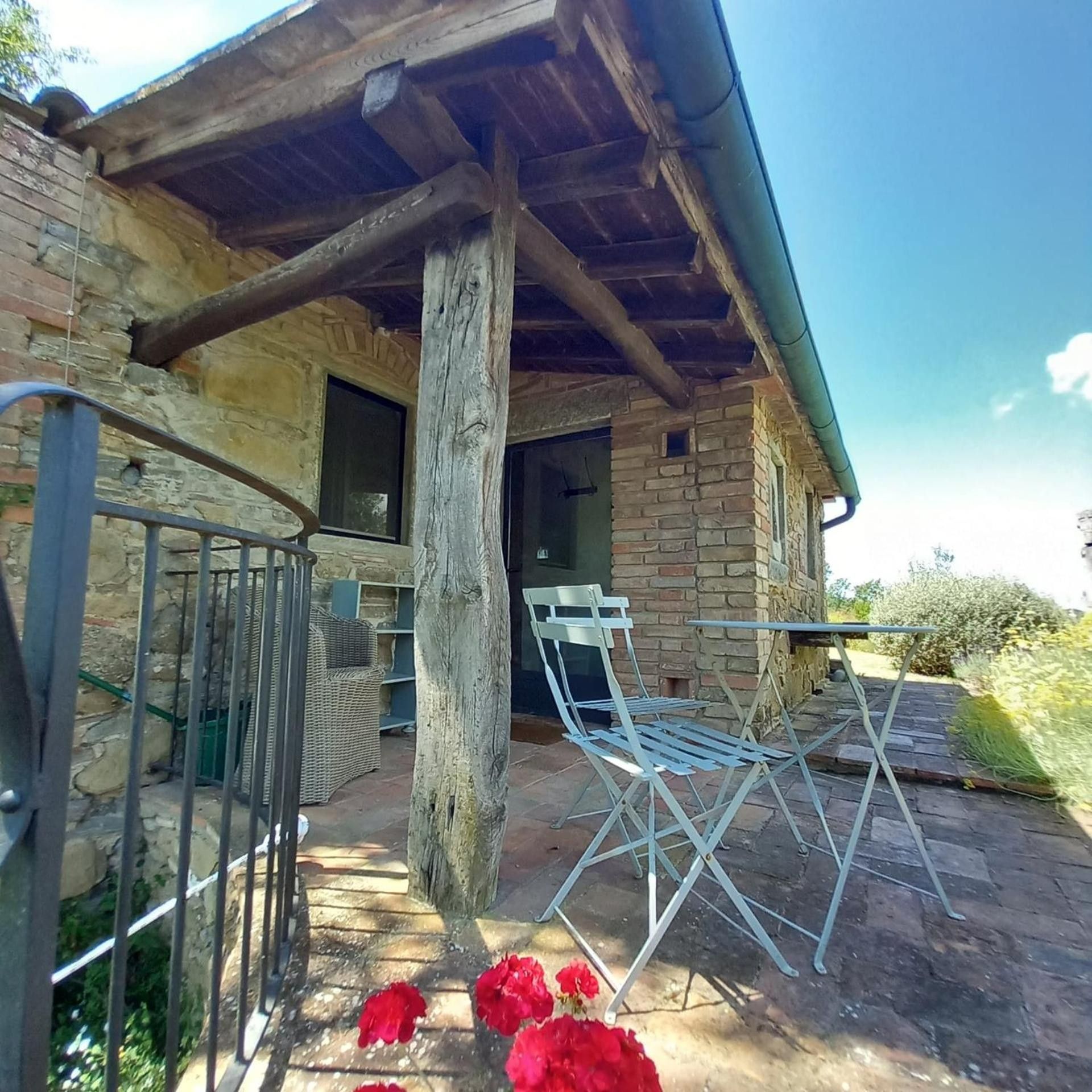 Un bâtiment rustique en pierre, doté d’un porche en bois, de chaises en métal et d’un portail en métal.