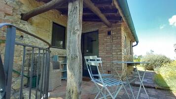 Un bâtiment rustique en pierre, doté d’un porche en bois, de chaises en métal et d’un portail en métal.