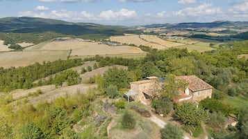 A stone building with a tiled roof surrounded by rolling hills and fields.