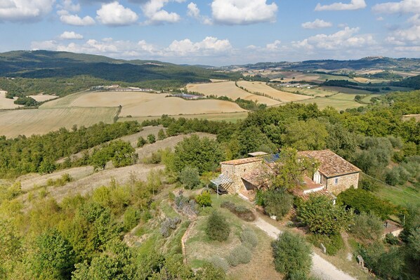 A stone building with a tiled roof surrounded by rolling hills and fields.