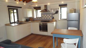A compact kitchen with white cabinets, a wooden countertop, a built-in oven, and a small dining table with a chair.