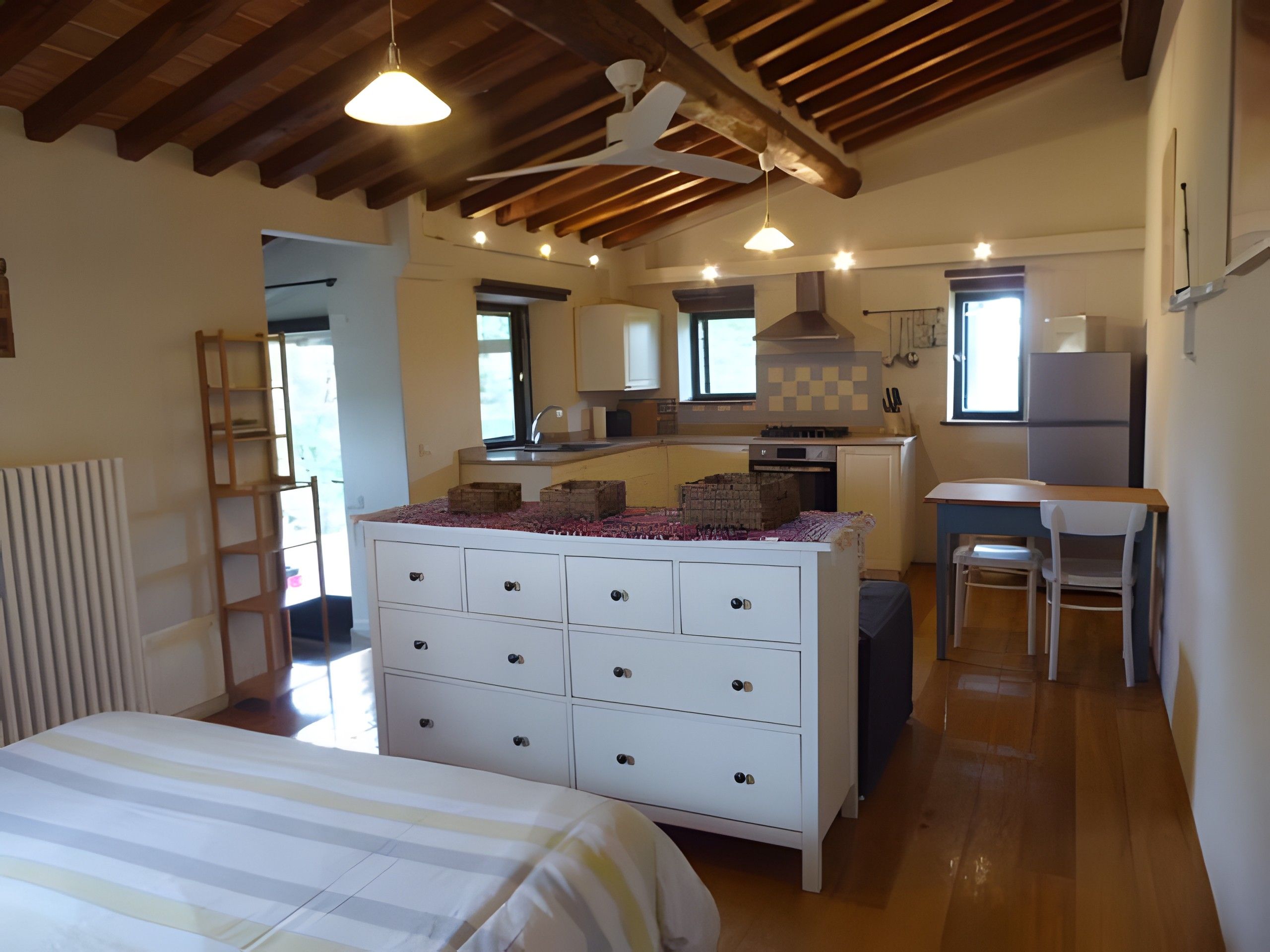 Een slaapkamer met een bed, een dressoir en een kitchenette met een fornuis en een spoelbak.
