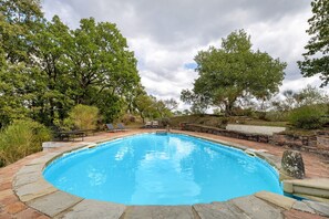 Una piscina con borde de ladrillo, rodeada de árboles y un muro de piedra.