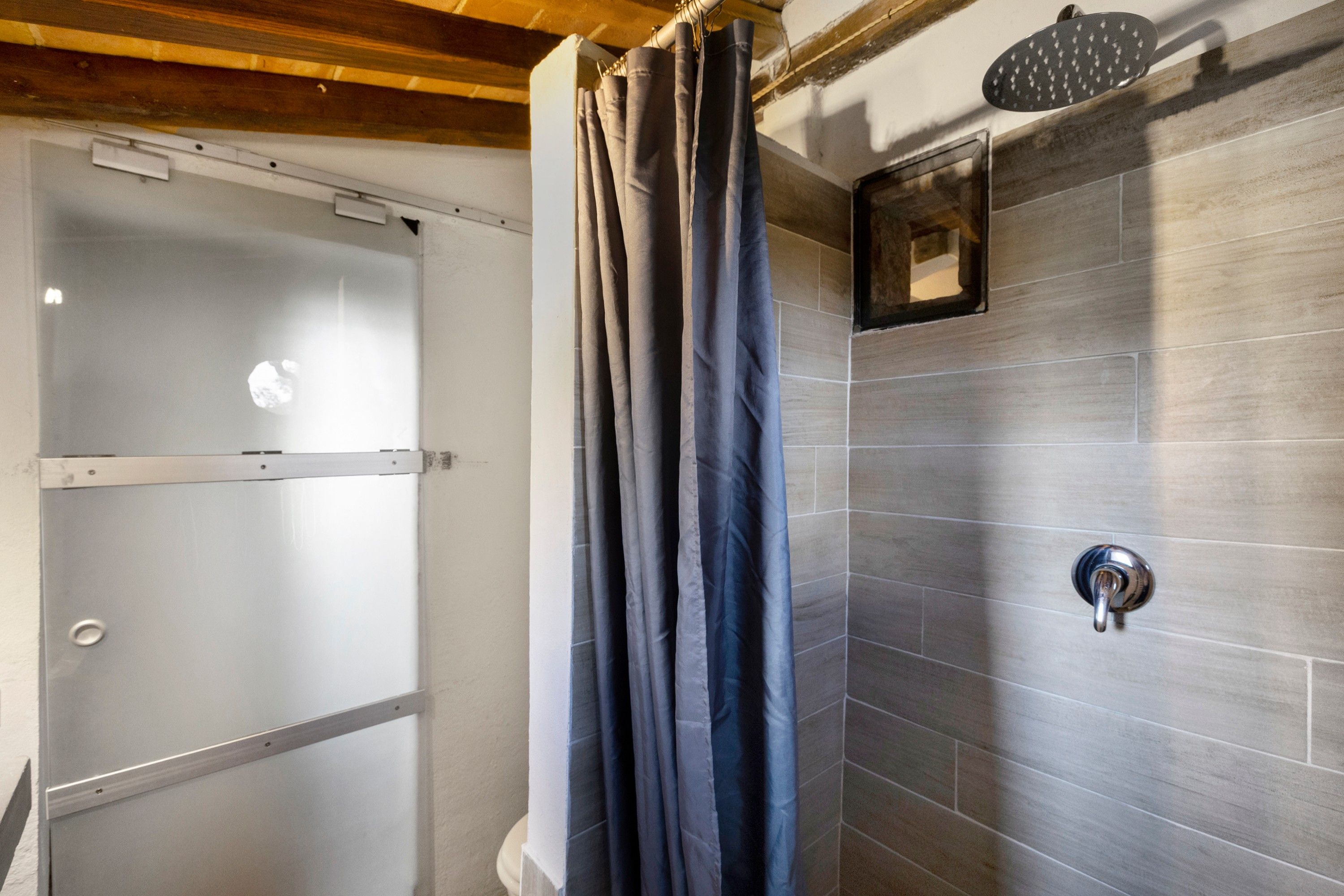 Un baño con ducha, puerta de vidrio y pared con azulejos.