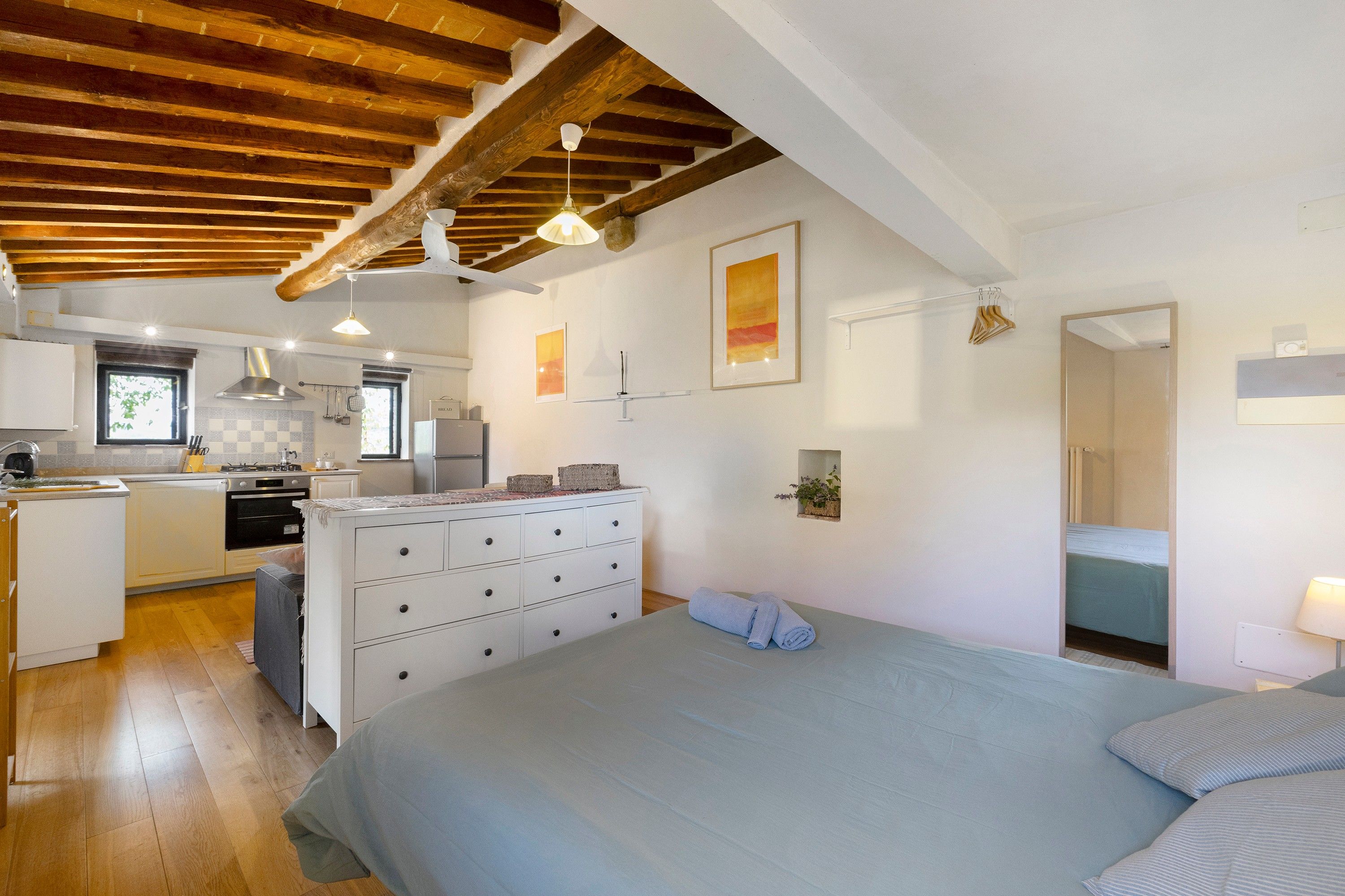 A bedroom with a bed, a dresser, and a view of the kitchen.
