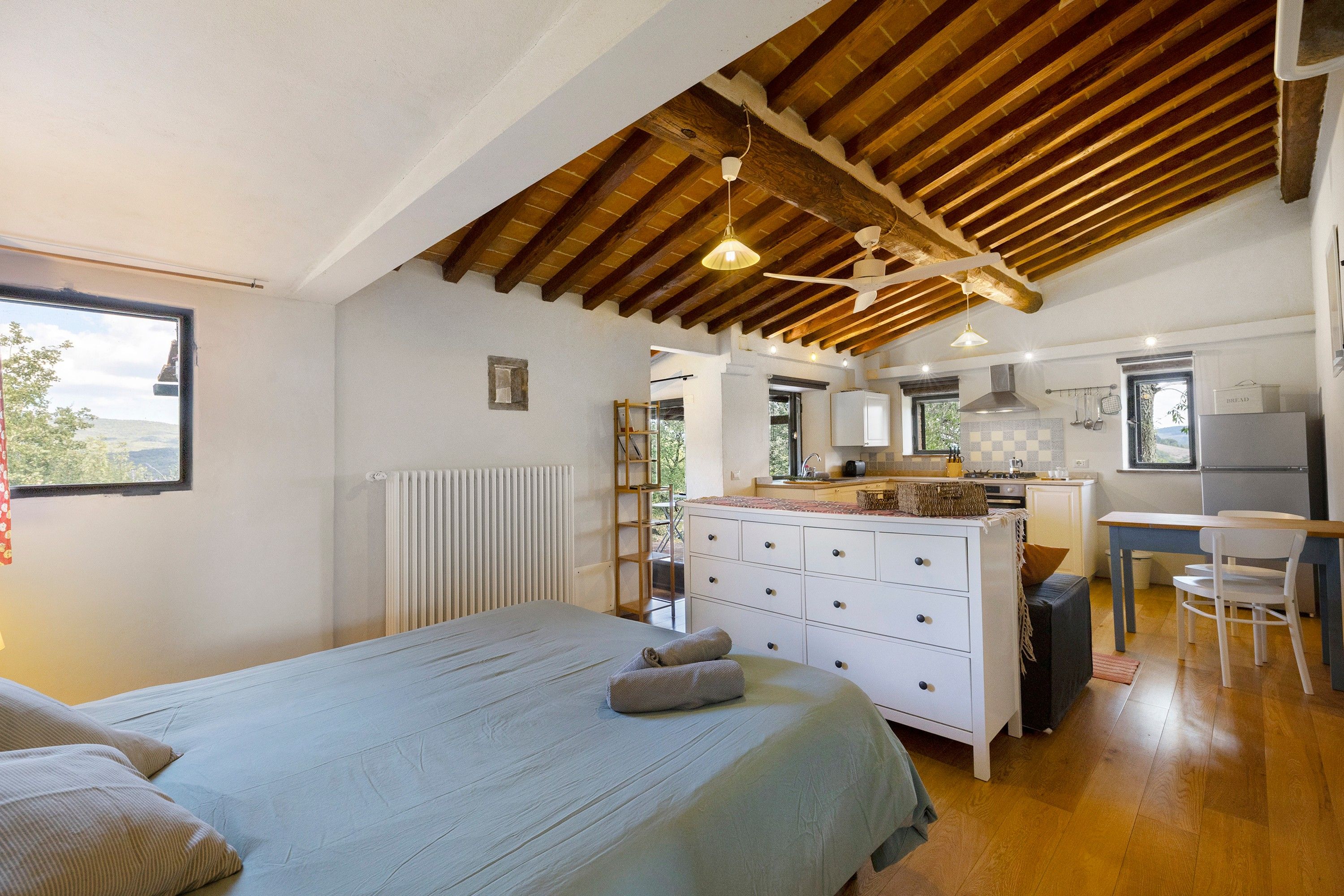 Une chambre avec un lit, une commode et une vue sur un coin cuisine.