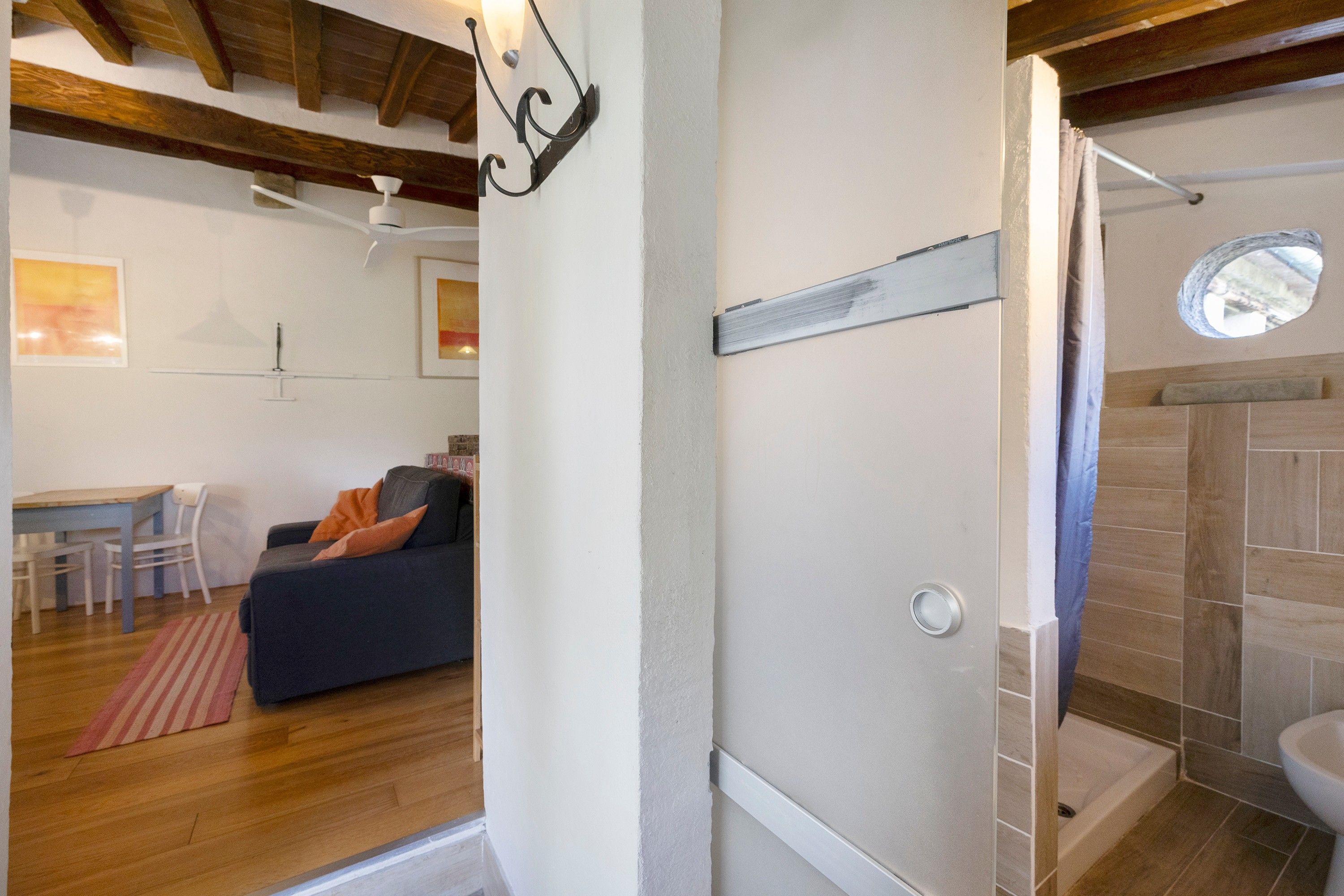 Une pièce avec un plafond en bois, un mur blanc, un canapé noir avec des coussins orange, une petite table avec des chaises et une fenêtre donnant sur un paysage agréable.