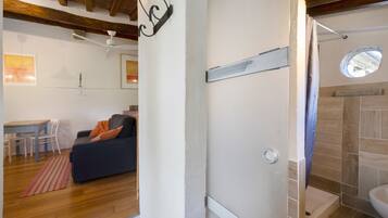 Une pièce avec un plafond en bois, un mur blanc, un canapé noir avec des coussins orange, une petite table avec des chaises et une fenêtre donnant sur un paysage agréable.