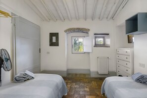 A bedroom with two beds, a radiator, a dresser, and a window with a view of greenery.