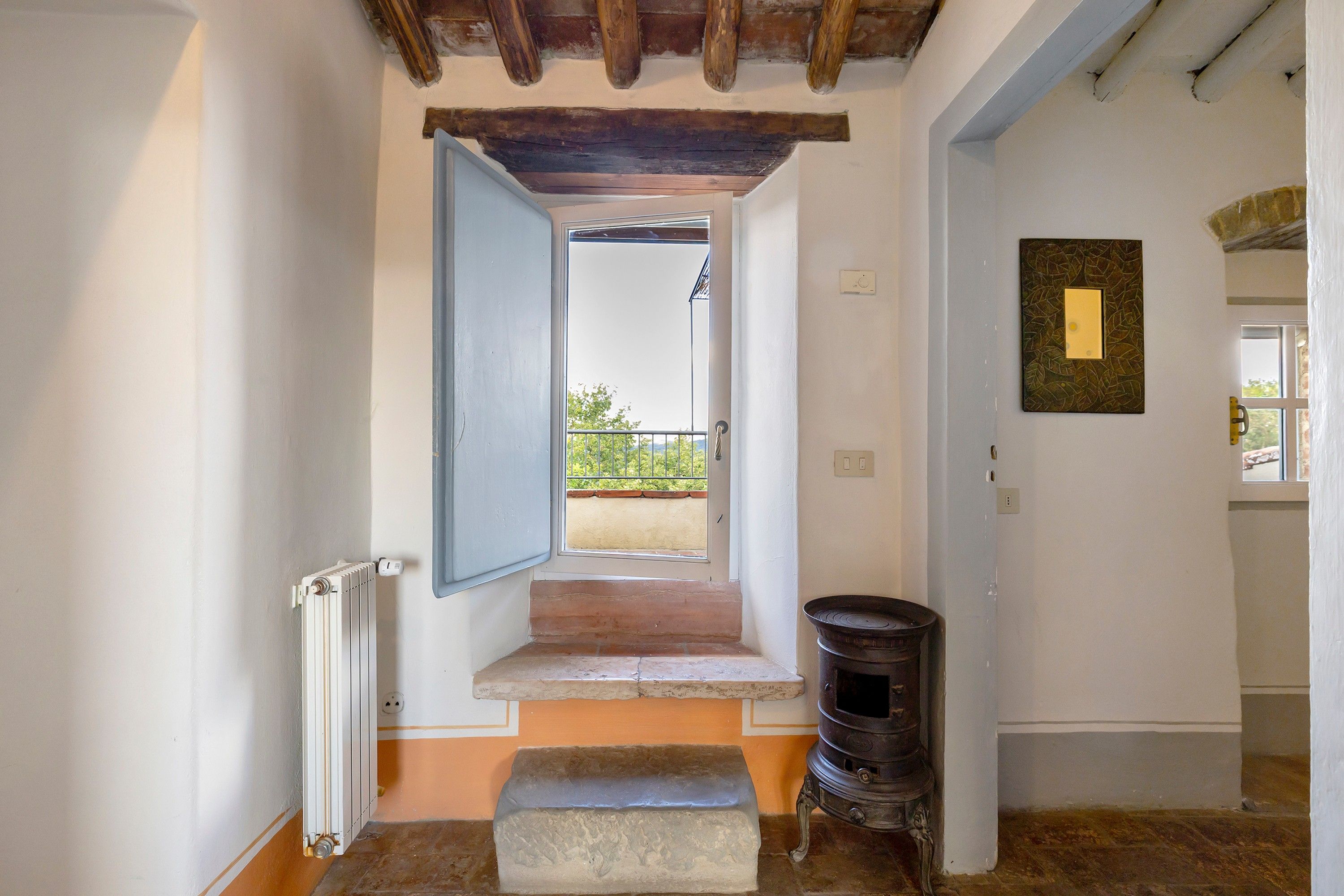 Een trap naar een buitenbalkon met uitzicht, een radiator, een stenen bank en een traditionele houtkachel.