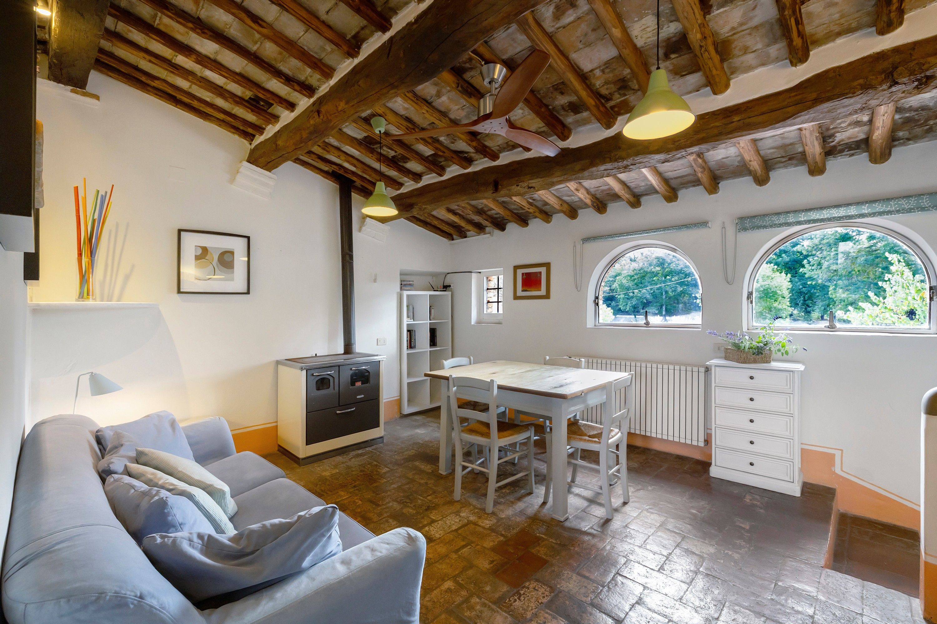 A cozy kitchen with a dining table, a built-in oven, and a window with a view of trees.