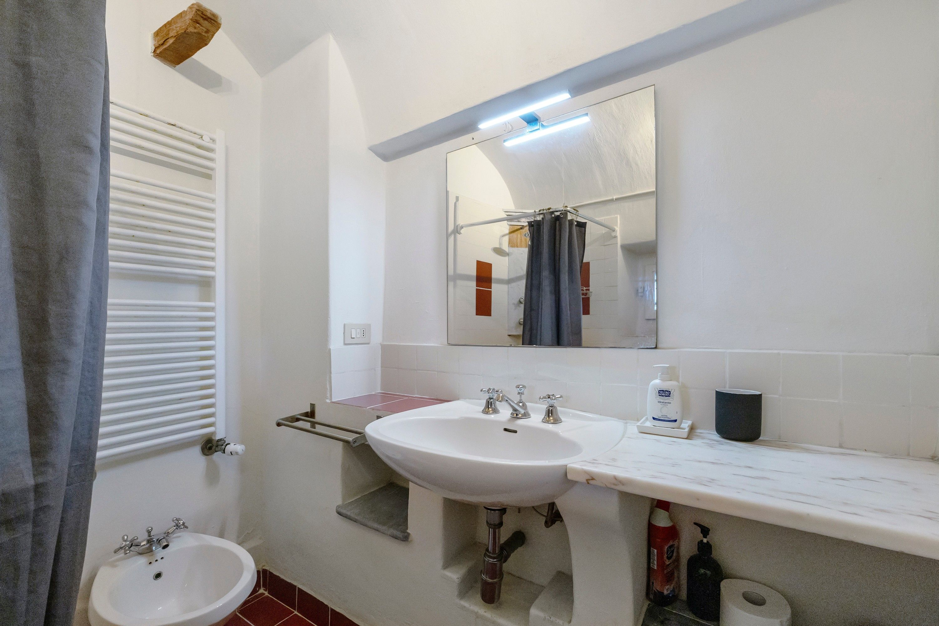 Un baño con un lavamanos blanco, un espejo encima y un perchero para toallas.