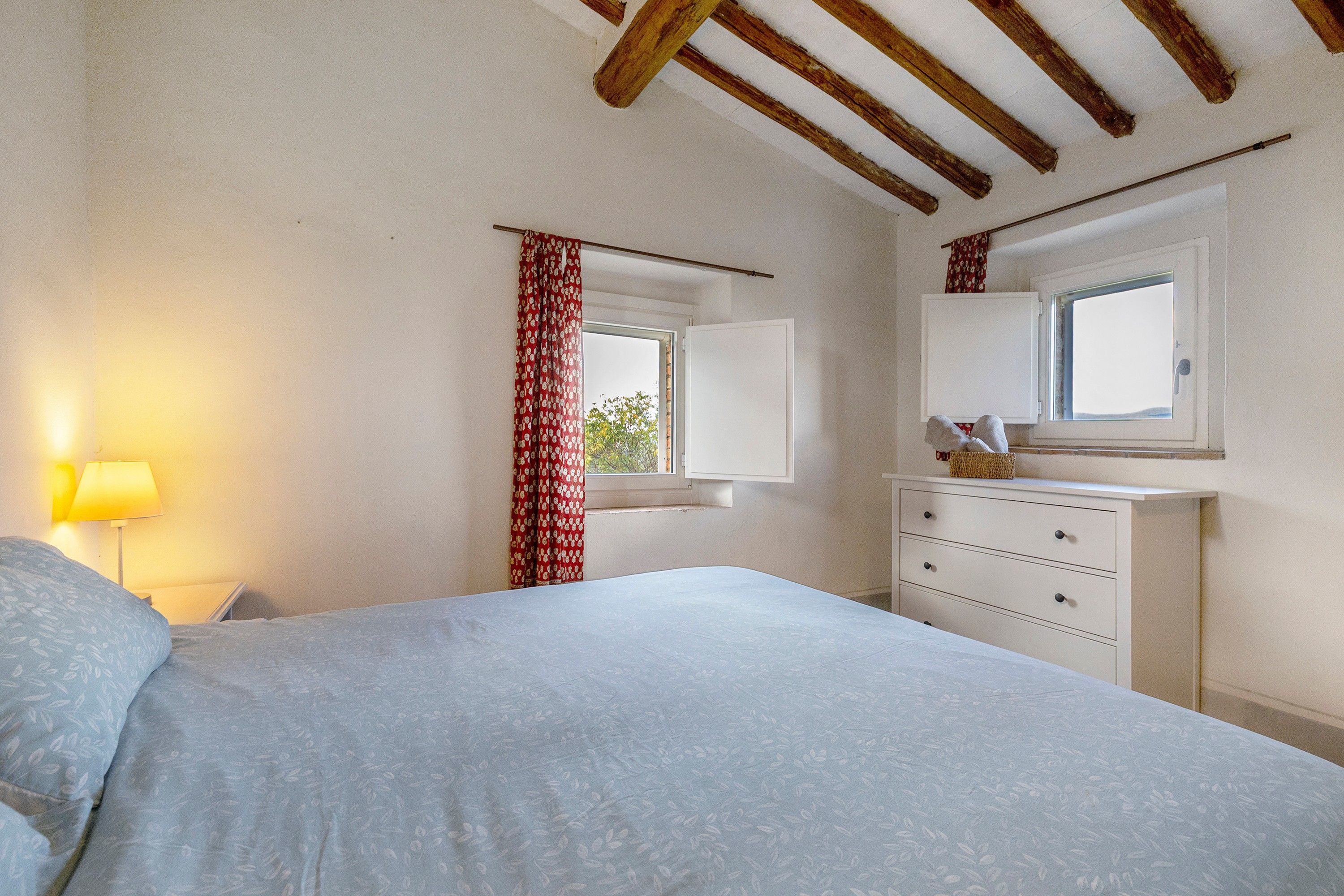 A bedroom with a bed, a dresser, a window with a view, and a lamp.