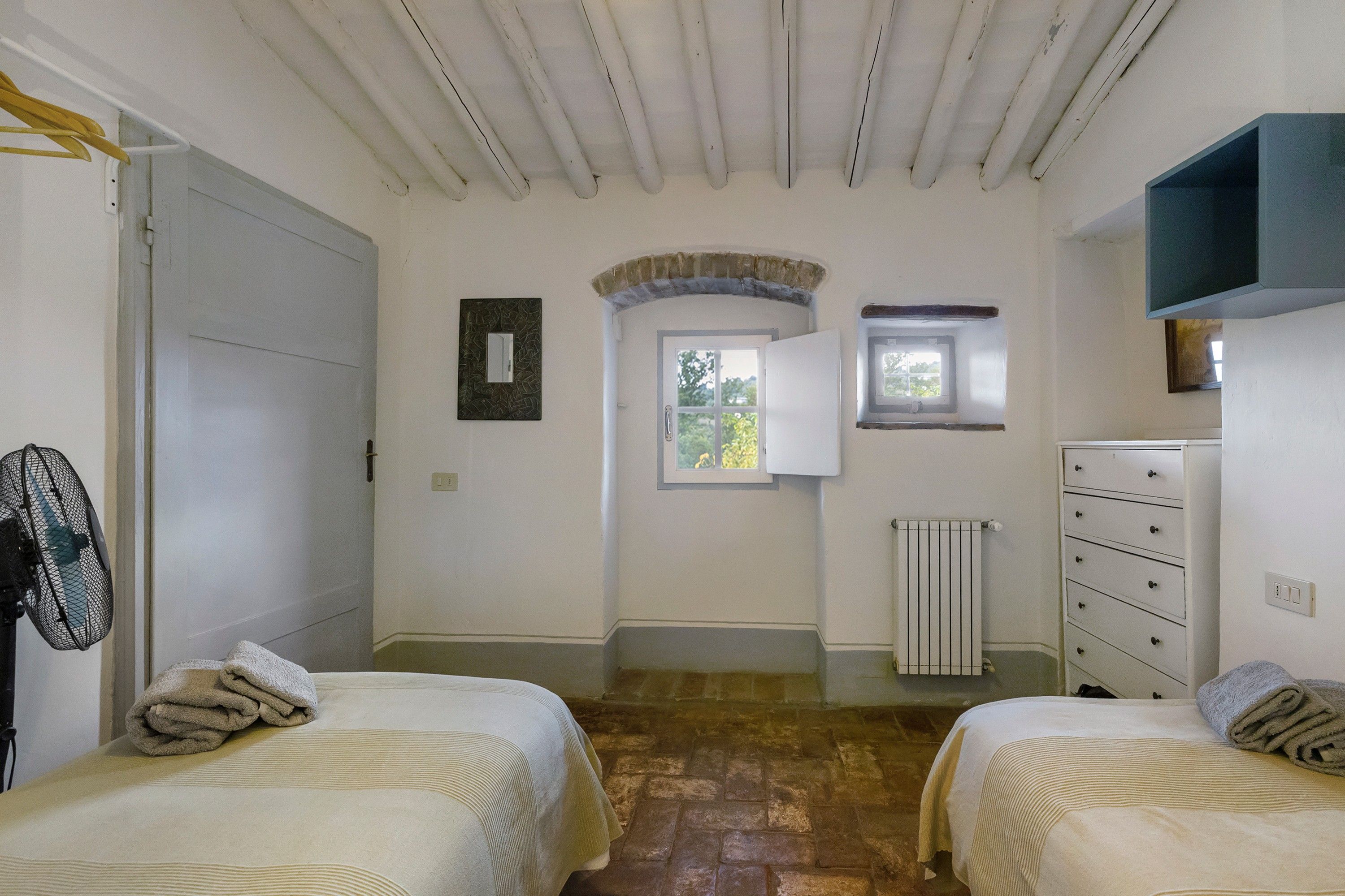 A bedroom with two beds, a dresser, a radiator, a window, and a door.