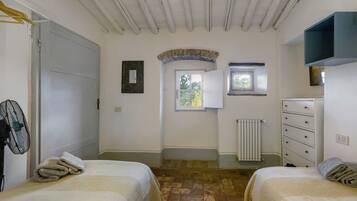 A bedroom with two beds, a dresser, a radiator, a window, and a door.