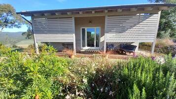 Une maison de plain-pied dotée d’un porche couvert, d’une porte-fenêtre coulissante et d’un petit espace extérieur aménagé pour s’asseoir.