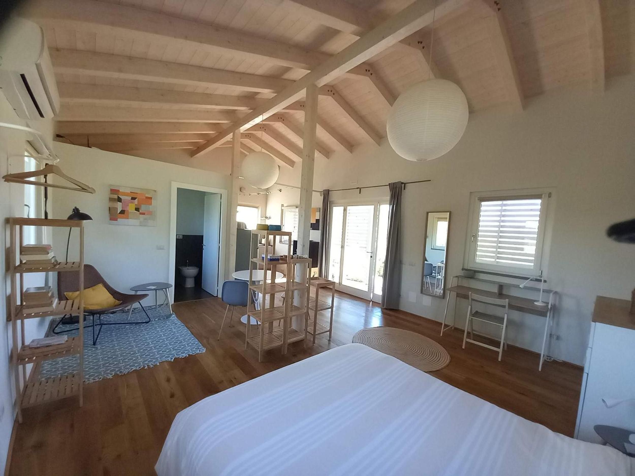 Une chambre spacieuse avec un grand lit, un plancher en bois et un plafond avec des poutres apparentes.