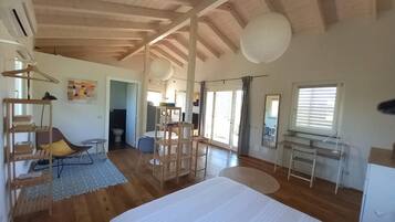 Une chambre spacieuse avec un grand lit, un plancher en bois et un plafond avec des poutres apparentes.
