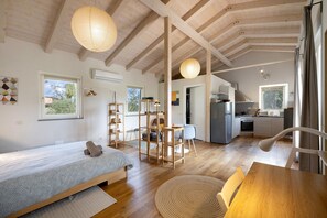 Un dormitorio acogedor con cama, un escritorio de madera y una mesa de comedor. Cuenta con una zona de cocina con refrigerador y estufa.