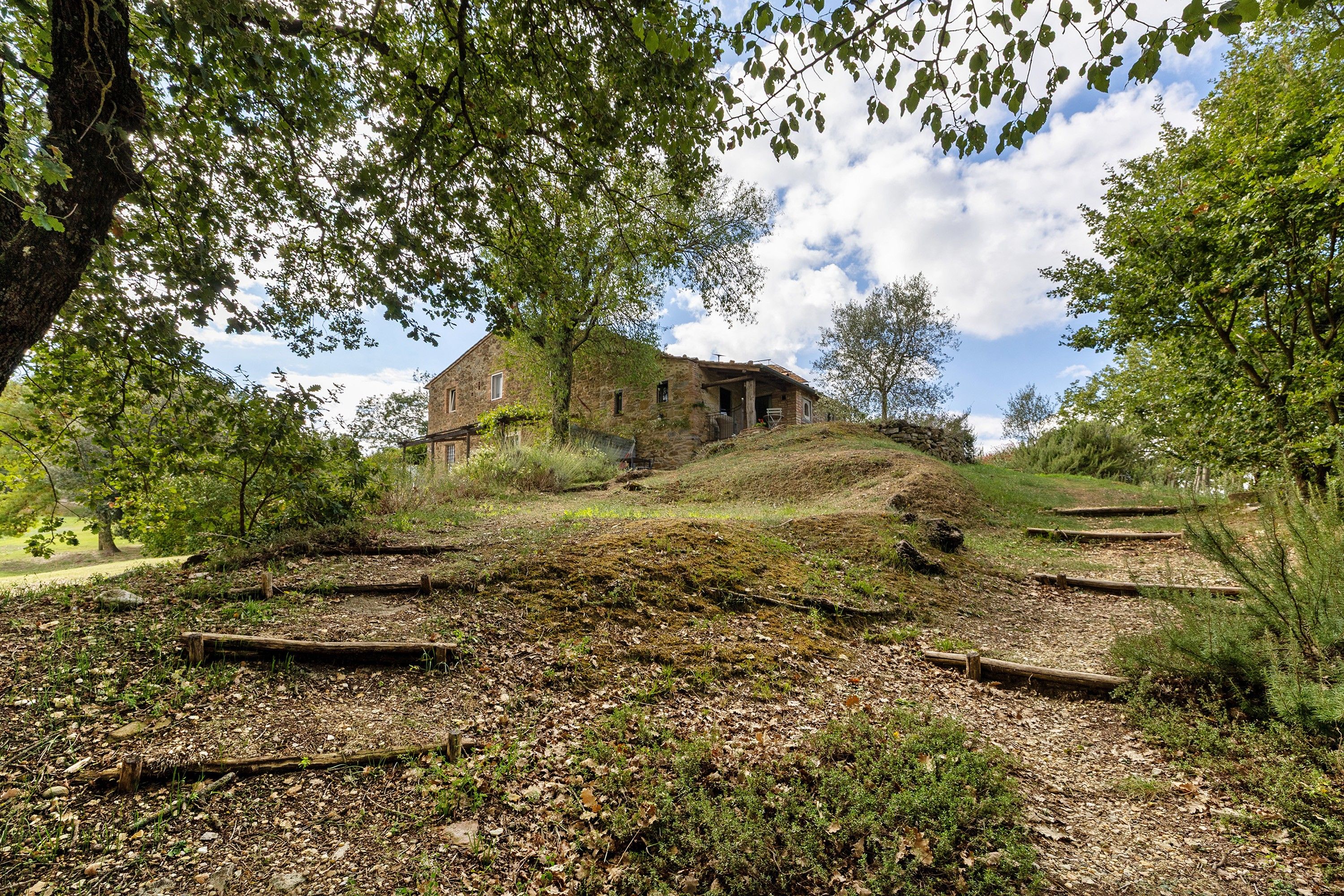 Un edificio de piedra con techo inclinado, rodeado de árboles y un césped con un sendero que lo lleva a él.