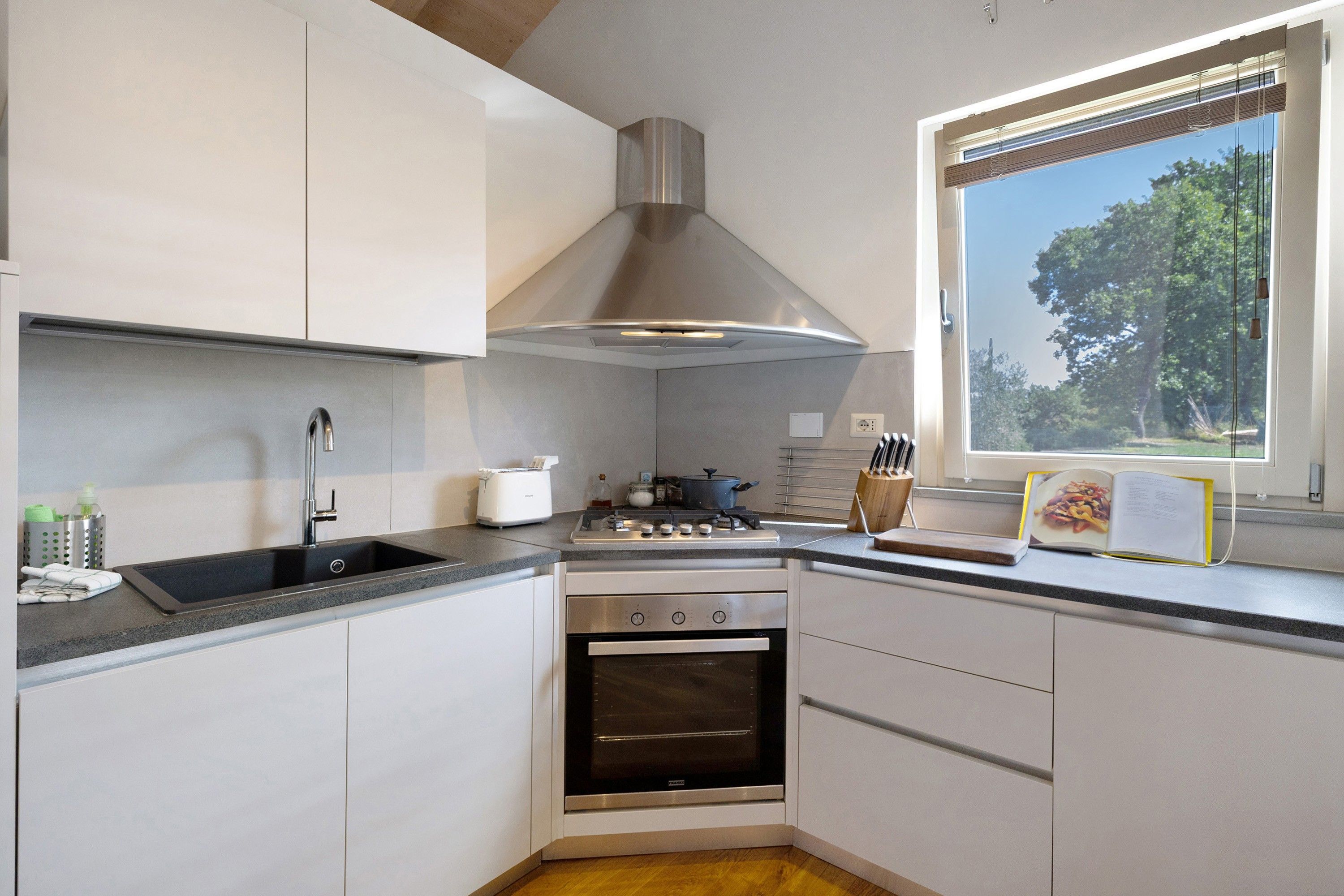 Een moderne keuken met een roestvrijstalen afzuigkap, een inbouwoven en een raam met uitzicht op bomen.