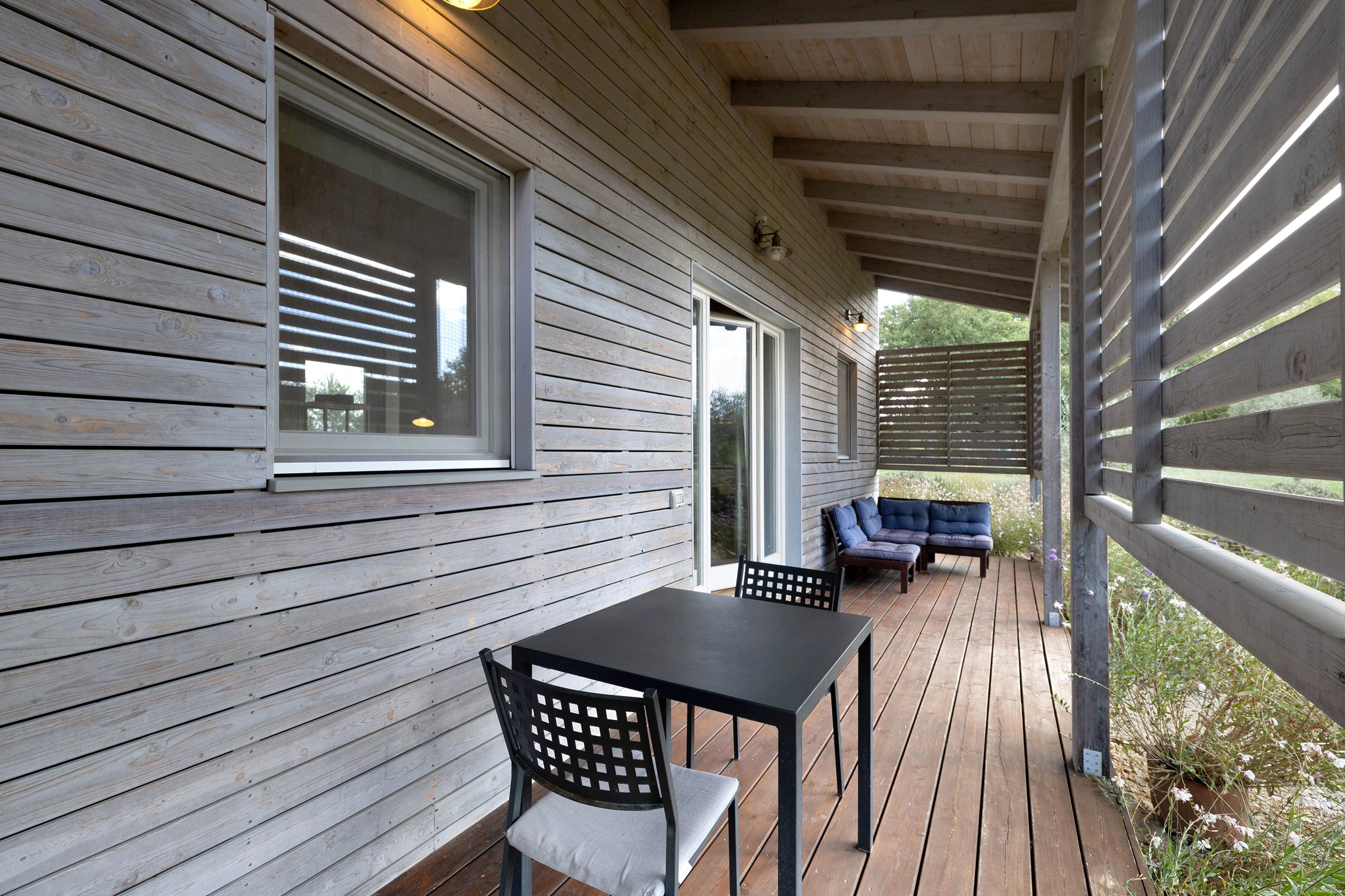 Un espace extérieur abrité, doté d’une terrasse en bois, d’une table avec une chaise et d’un canapé.