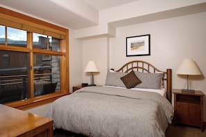 A bedroom with a bed, two bedside tables, a window with blinds, and a framed picture on the wall. - Luxury 2 Bed, 2 Bath, Capitol Peak, In the heart of Base Village, steps to lift! (Snowmass Village)