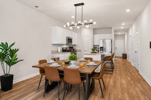 Une cuisine moderne avec des meubles blancs, un îlot central et un coin repas comprenant une table en bois et des chaises marron.